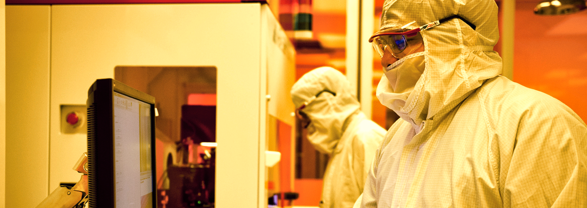 Photo of two people in clean room garb working on a machine tool.