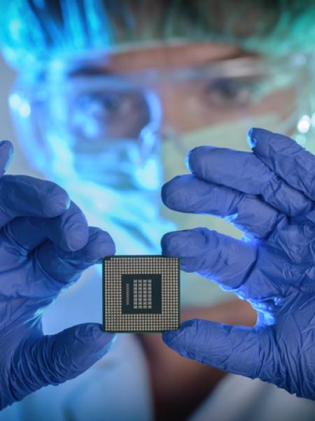 Technician in clean room garb holding a semiconductor device