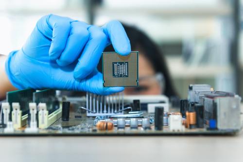 technician holding a microprocessor over a microelectronics board